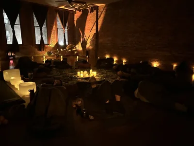 A candlelit Aloka session at Bodha Yoga: brick walls, tall windows, crystal bowls glowing on the floor